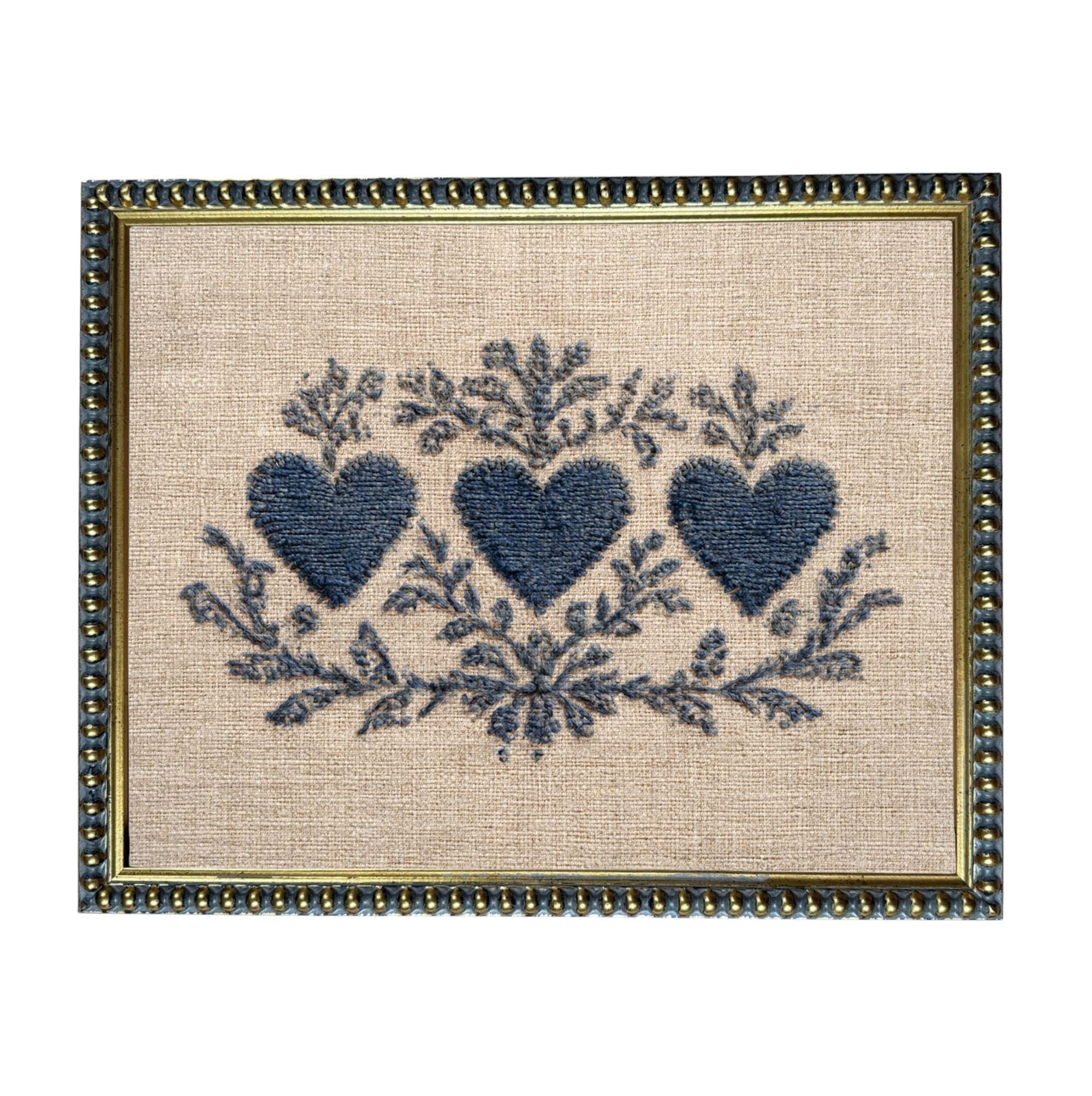 a framed embroidered design with three blue hearts and floral elements.
