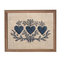 a square frame with a beige background and a decorative border. The frame contains a blue floral design with three blue hearts arranged in a symmetrical pattern.