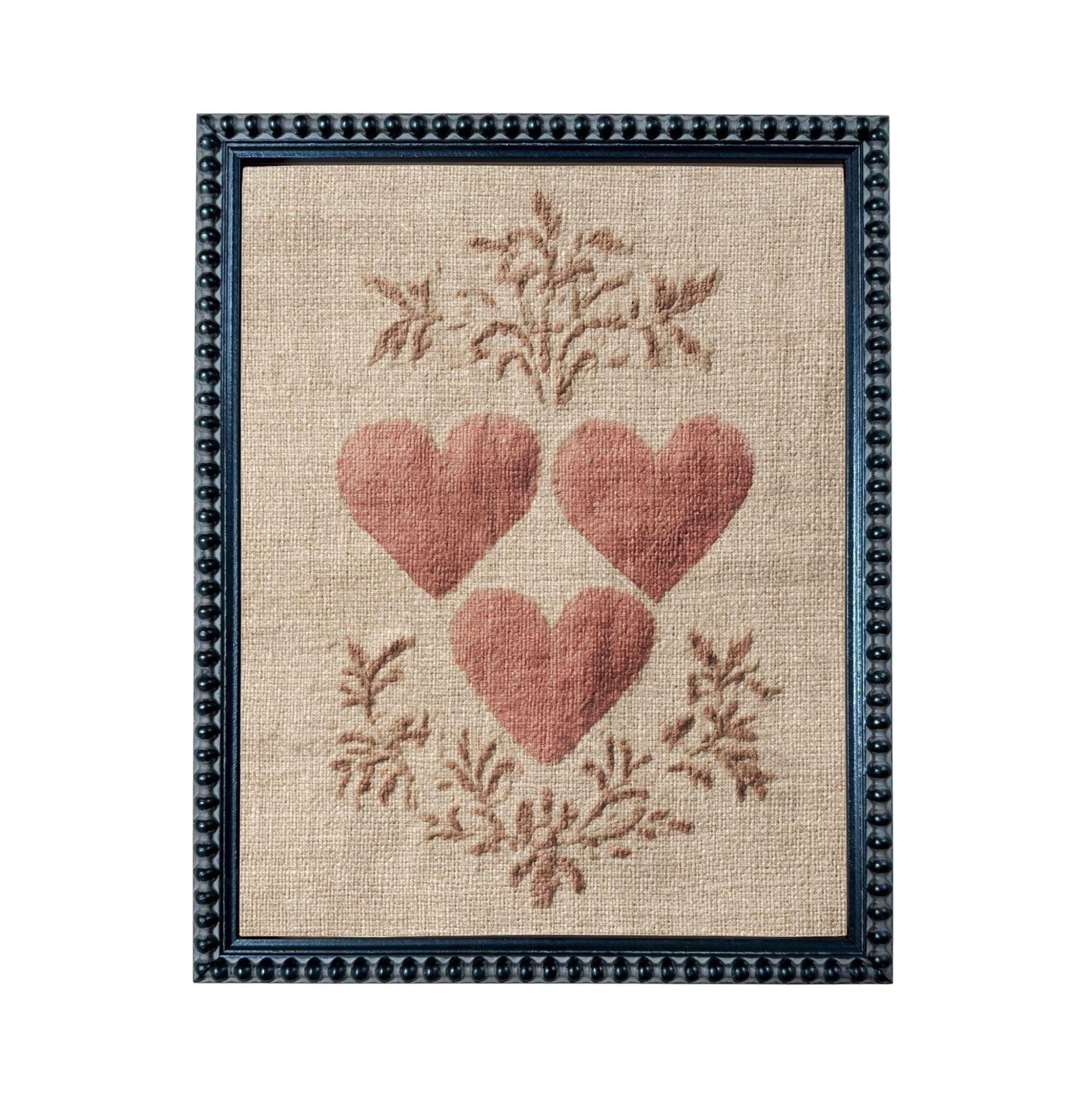 a framed piece of artwork with a beige background and a floral design. The artwork is framed in a black frame with a decorative border. The artwork displays three red hearts arranged in a circular pattern, surrounded by a floral design.