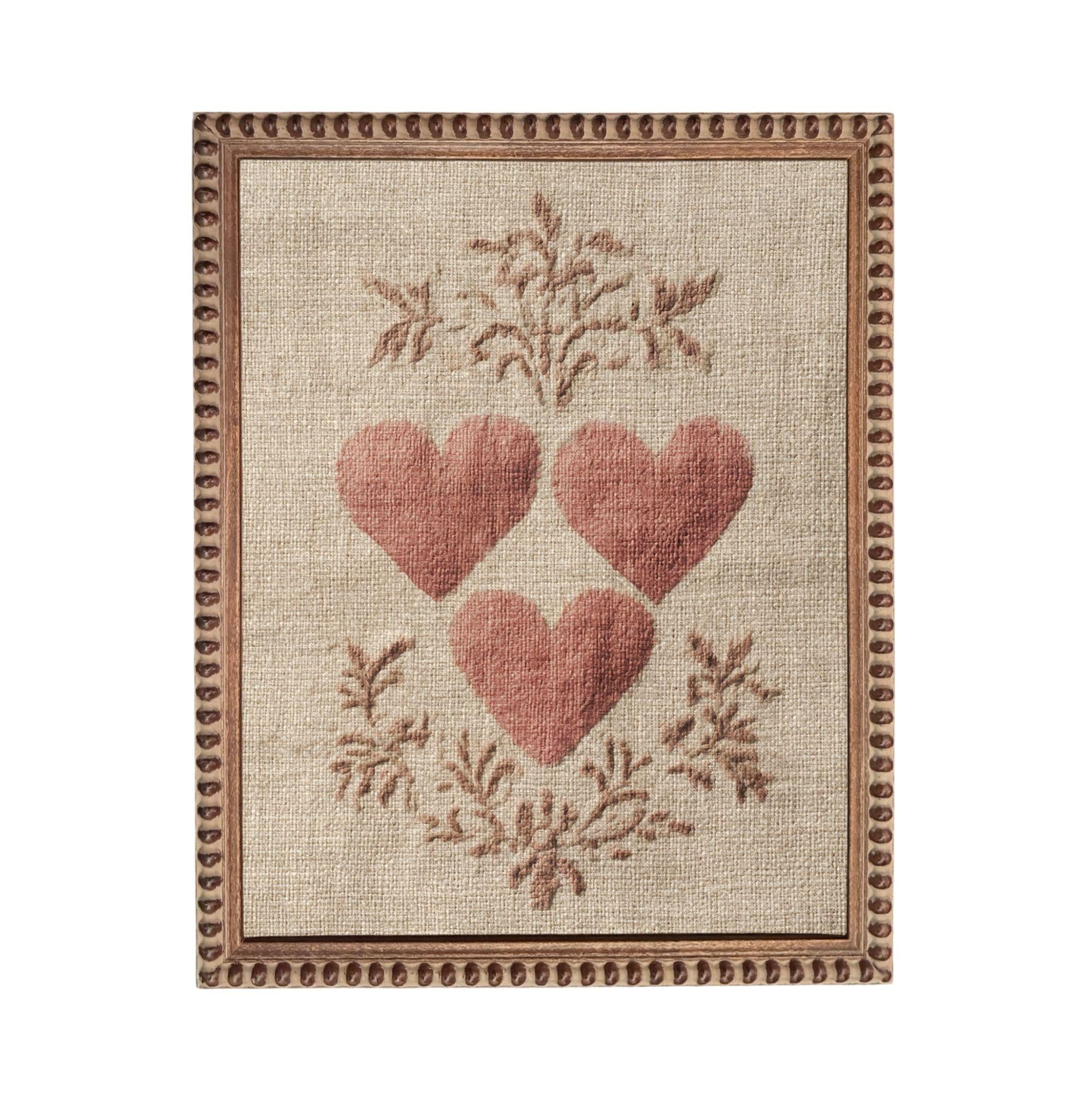 a beige fabric with a decorative border and three red heart-shaped embroidered designs.