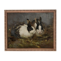 Two rabbits sitting in a grassy area, surrounded by hay.
