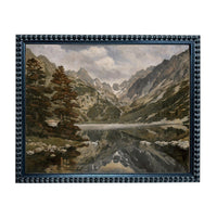 The image is a framed painting depicting a serene mountain landscape with a lake or river in the foreground, surrounded by trees and mountains.